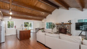 A spacious living area with a wooden ceiling, a stone fireplace, a large white sofa, and a television.
