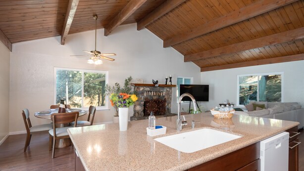 A spacious kitchen with a large island, wooden ceiling beams, and a stone fireplace.