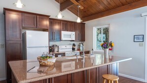A kitchen with dark wood cabinets, a white refrigerator, a microwave, a stove, and a large island with stools.