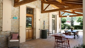 An open patio with stone flooring, wooden beams, wicker furniture, and a view of greenery. - Gîtes de France® - Gîte du Chateau Saint Didier (PARNAC)