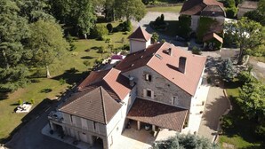 A large stone building with a red-tiled roof, surrounded by greenery and other residential structures. - Gîtes de France® - Gîte du Chateau Saint Didier (PARNAC)