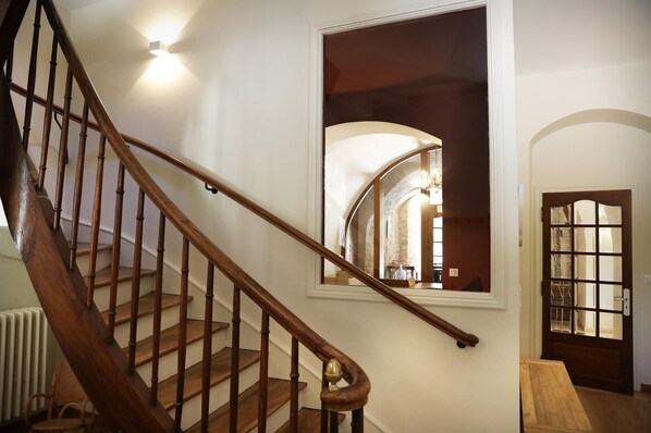 Una escalera de madera con barandilla, una pared blanca y una puerta con paneles de vidrio.