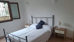 A single bed with a metal frame, white bedding, and a blue pillow. There are two bedside tables with lamps. The room has a tiled floor and a window with a metal grill. - Panorama Residence swimming pool 2 bedrooms (San Giovanni)