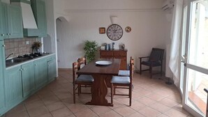 A kitchen with teal cabinets, a wooden dining table with chairs, a clock on the wall, and a window with curtains. - Panorama Residence swimming pool 2 bedrooms (San Giovanni)