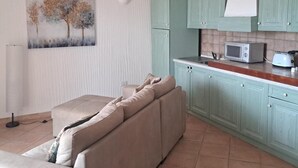 A living room with a beige sofa, a painting of trees, and a kitchen with teal cabinets and a microwave. - Panorama Residence swimming pool 2 bedrooms (San Giovanni)