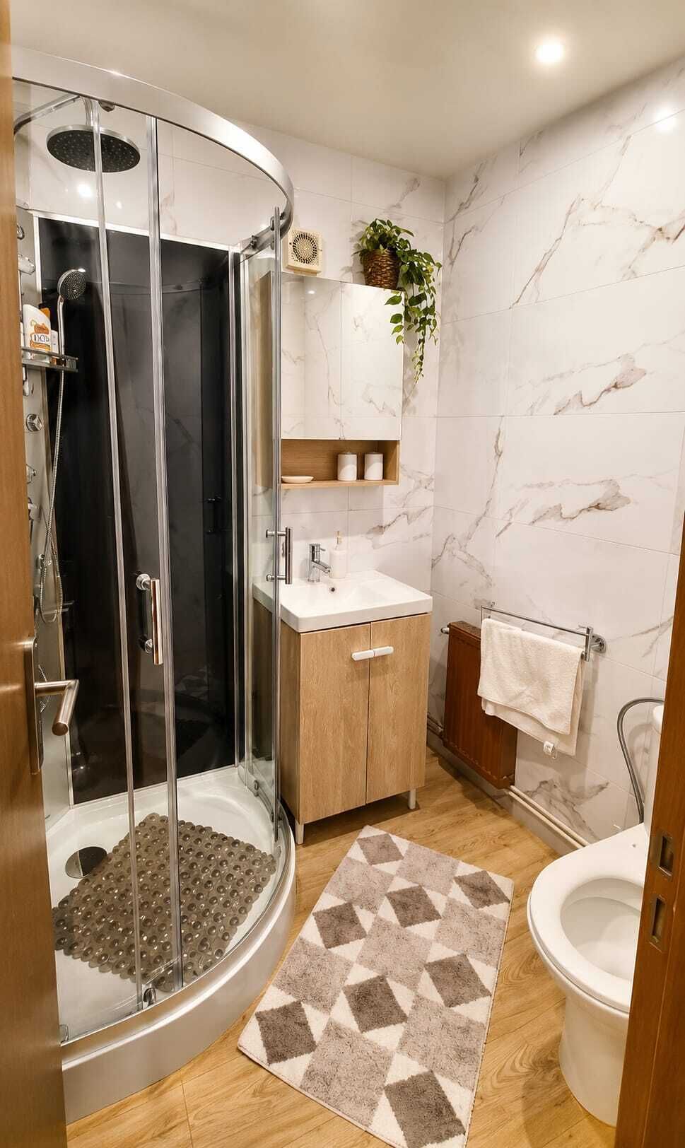 A modern bathroom with a glass-enclosed shower, a wooden vanity, marble walls, and a patterned rug.