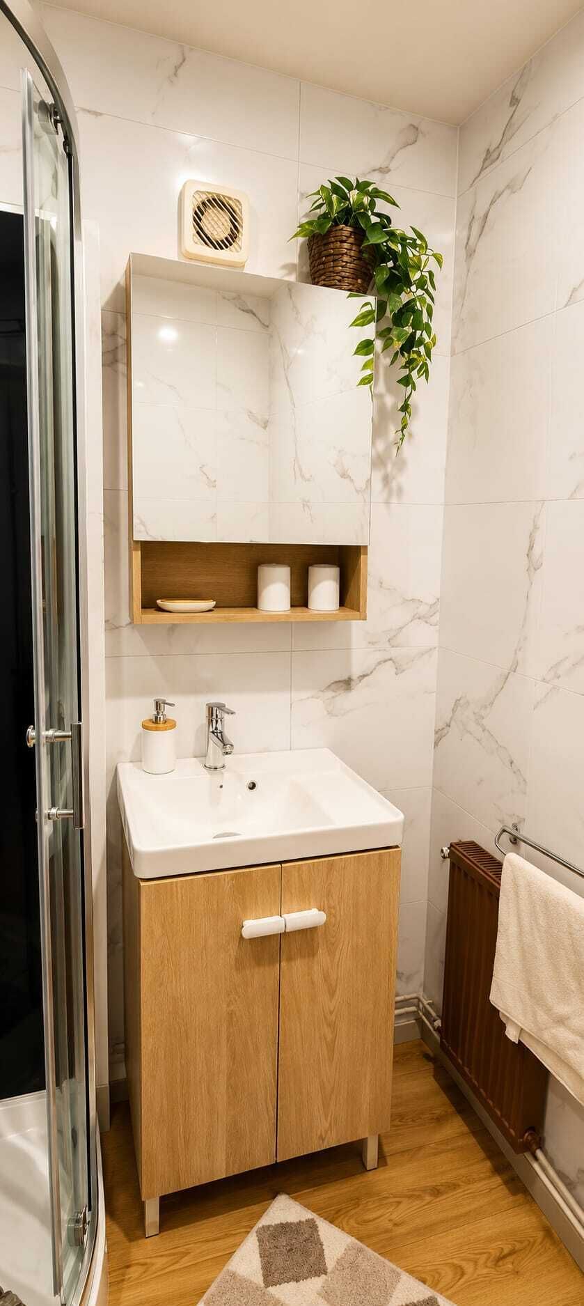 A bathroom with a white sink, wooden cabinet, marble walls, a hanging plant, and a towel rack.