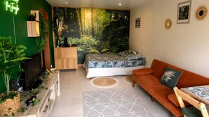 Quarto com cama, sofá, televisão e parede verde com mural de floresta.