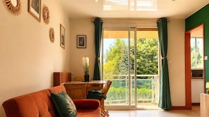 Uma sala de estar com sofá, mesa de jantar e vista através de uma porta de vidro.