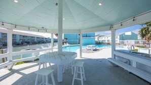 A covered outdoor area with a pool, white furniture, and a view of buildings in the background. - Waterfront Luxury Condo (Rockport)