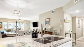 A modern kitchen with granite countertops, a double sink, and a dining area with a round table and chairs. - Waterfront Luxury Condo (Rockport)