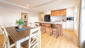 Une cuisine moderne avec des meubles en bois, un îlot central et un coin repas avec des chaises blanches.