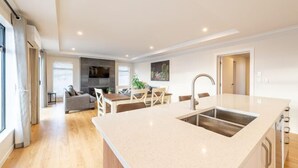 Une cuisine moderne dotée d’un grand îlot central, un coin repas avec une table et des chaises, et un salon avec un canapé et un téléviseur.