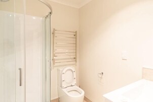 A bathroom with a glass shower enclosure, a toilet with a towel rail, and a sink.