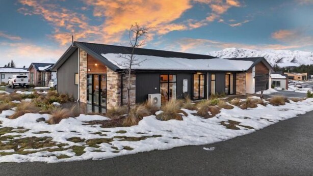 Un bâtiment moderne à la façade en pierre et aux grandes fenêtres, entouré de neige et dominé par un paysage montagneux.
