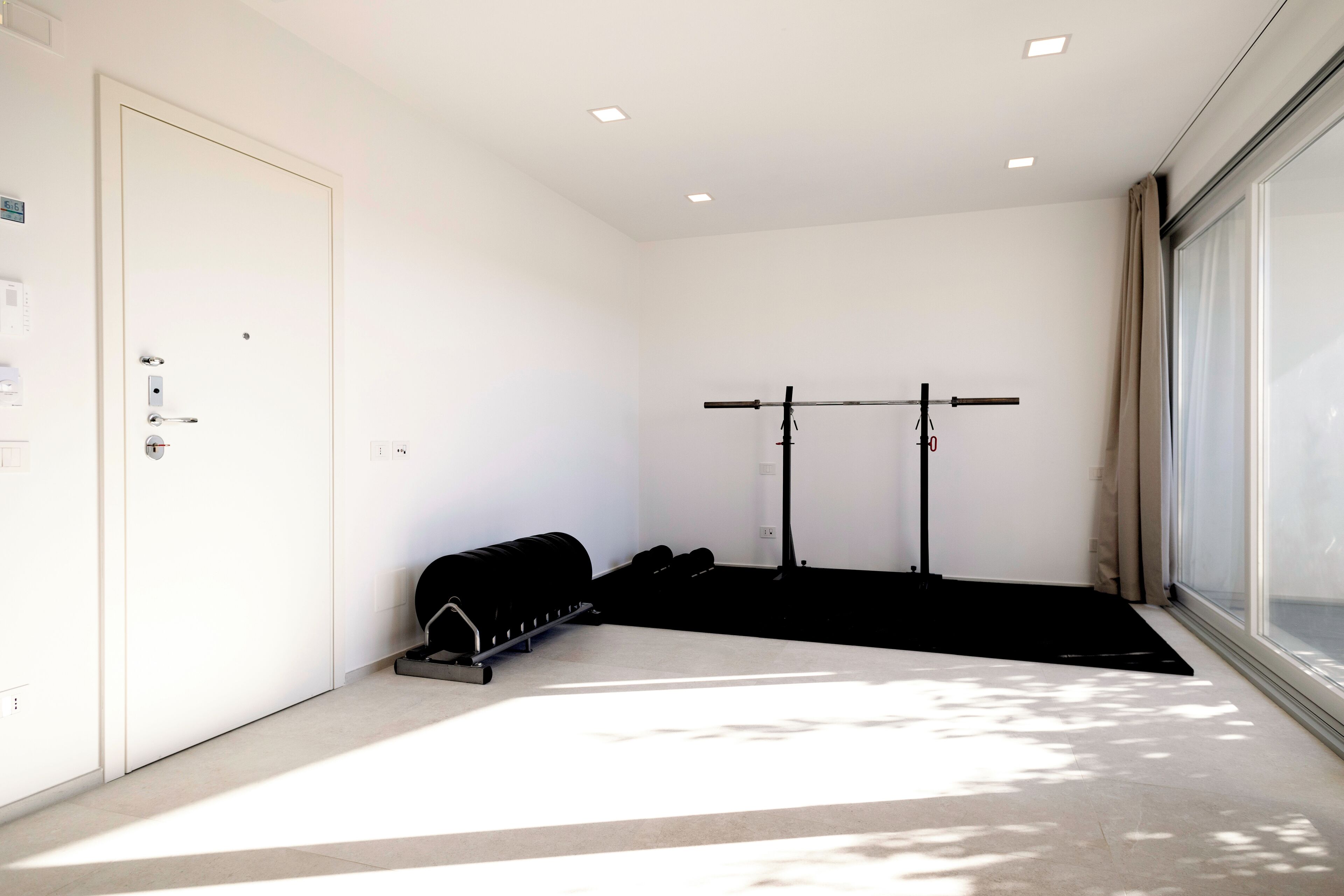 A room with a door, a window, a pull-up bar, and a black mat.