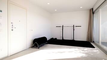 A room with a door, a window, a pull-up bar, and a black mat.
