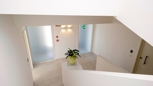 Rebedor modern d'hotel amb una escala, una planta en test i un senyal d'eixida d'emergència.