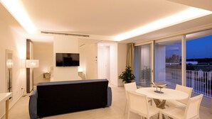 Un saló modern amb un sofà, una televisió, una taula de dinar amb cadires i un balcó amb vistes.
