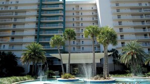 Un hôtel à étages, avec une enseigne bien visible portant l’inscription « Sterling Shores », et un espace piscine agrémenté de palmiers et d’un élément décoratif aquatique.