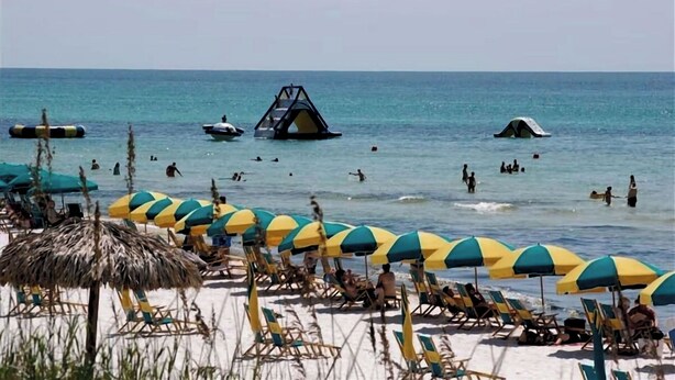 Une plage bordée de rangées de parasols et de chaises longues, avec une tour de surveillance pour les sauveteurs, et des gens qui nagent et se détendent dans l’eau.