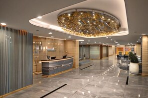 Un moderno vestíbulo de hotel con mostrador de recepción, un llamativo elemento decorativo en el techo y un suelo de mármol pulido.