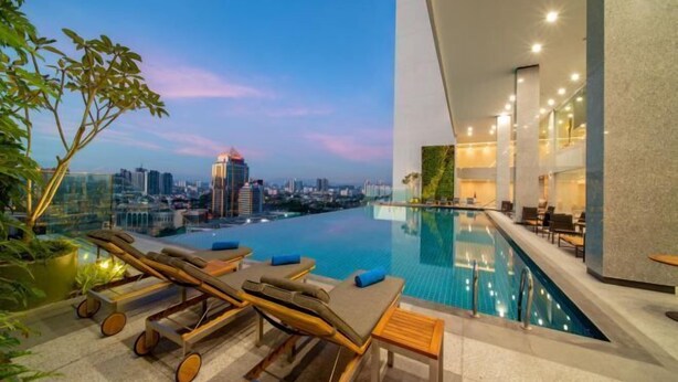 An infinity pool with lounge chairs and a city view at dusk. - Sunway Sanctuary - Seniors Hotel & Residences (Subang Jaya)
