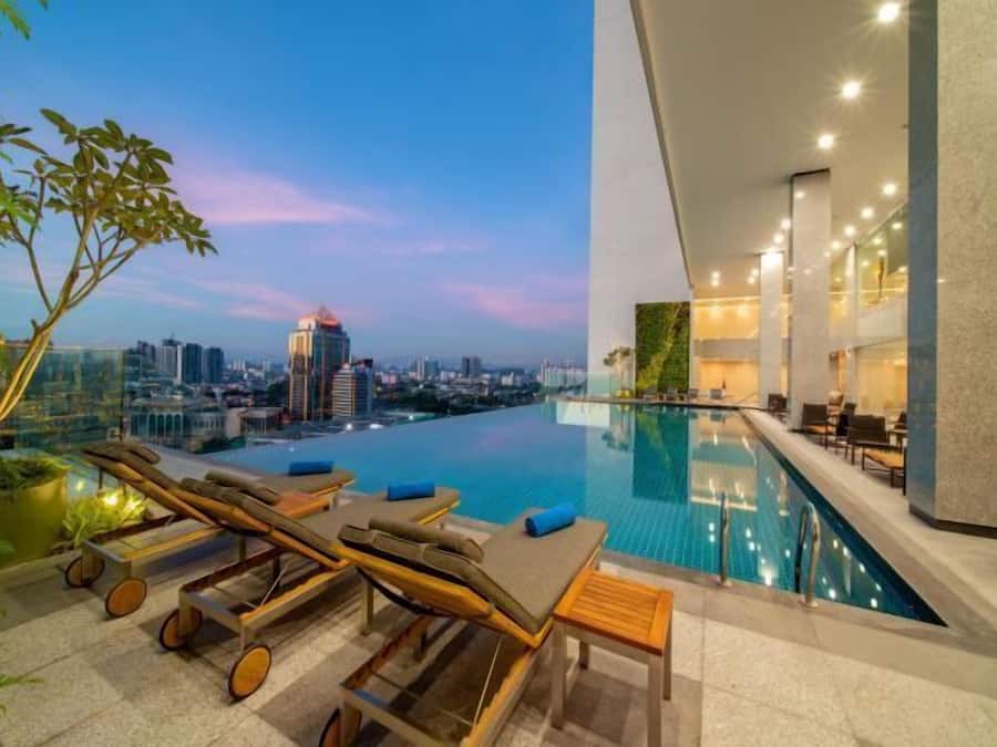 Una piscina infinita con sillones de descanso y vistas a la ciudad al anochecer.