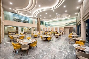 Un comedor amplio con varias mesas y sillas, un techo alto con iluminación singular y vistas al nivel superior a través de barandas de vidrio.
