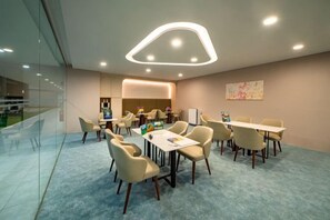Una sala de conferencias moderna con un separador de vidrio, sillas color beige, una mesa blanca y una lámpara de techo de diseño único.