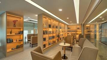 A modern library with bookshelves, comfortable seating, and a glass wall.