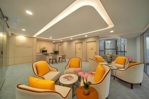A modern hotel lobby with seating areas, a reception desk, and a kitchen in the background.