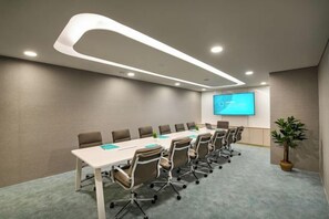 A conference room with a long table, chairs, a projector screen, and a potted plant.