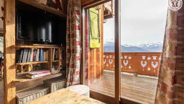 A cozy room with a wooden bookshelf, a television, and a view of snow-capped mountains through a glass door. - CHALET LE TREDARD - FEISSONS SUR SALINS (FEISSONS SUR SALINS)