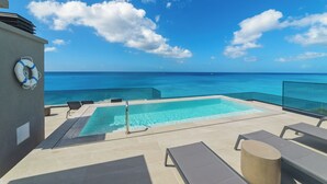An infinity pool with clear blue water, lounge chairs, and a lifebuoy on a balcony overlooking the ocean. - Allure 502. A stunning 2 Bedroom Beachfront Condo
with Breathtaking Ocean Views (St. Michael)