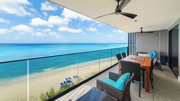A balcony with a view of the ocean, a table with chairs, and a ceiling fan. - Allure 502. A stunning 2 Bedroom Beachfront Condo
with Breathtaking Ocean Views (St. Michael)