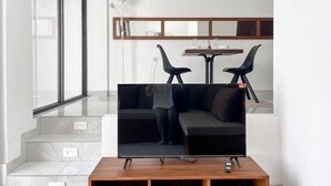 A modern living room with a flat-screen TV on a wooden stand, a black sofa, and a dining table with chairs. - The Lavana De Mello Villa Seminyak (1 Bedroom Villa with Private Pool) (Bali)