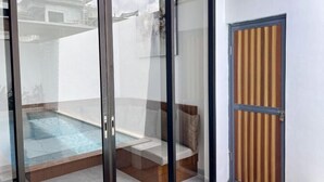 A glass-enclosed balcony with a pool, a wooden door, and a view of a building in the background. - The Lavana De Mello Villa Seminyak (1 Bedroom Villa with Private Pool) (Bali)