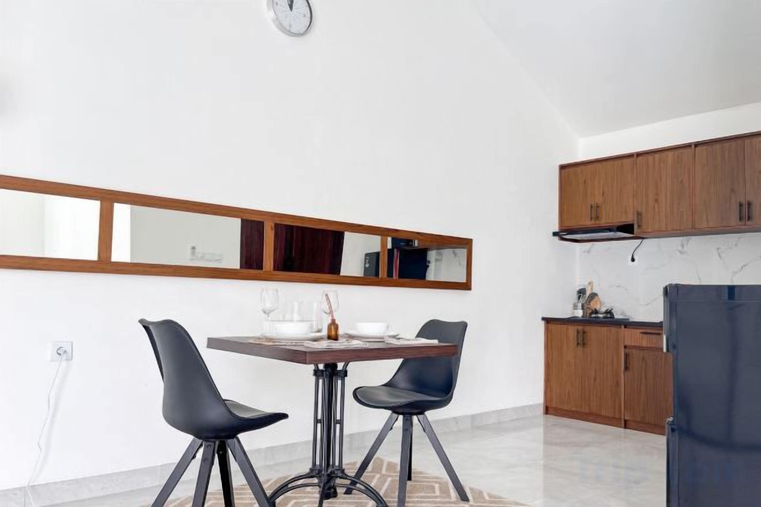 A modern kitchen with wooden cabinets, a dining table with two chairs, and a large mirror above the table.