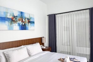 A hotel room with a bed, a nightstand, a lamp, a painting, and a large window with curtains. - The Lavana De Mello Villa Seminyak (1 Bedroom Villa with Private Pool) (Bali)