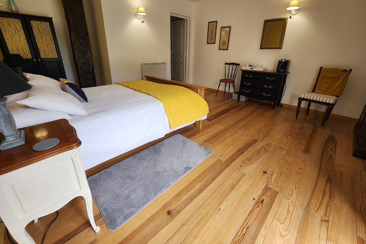 Un dormitorio con cama, mesita de noche, cómoda, silla y escritorio con lámpara.