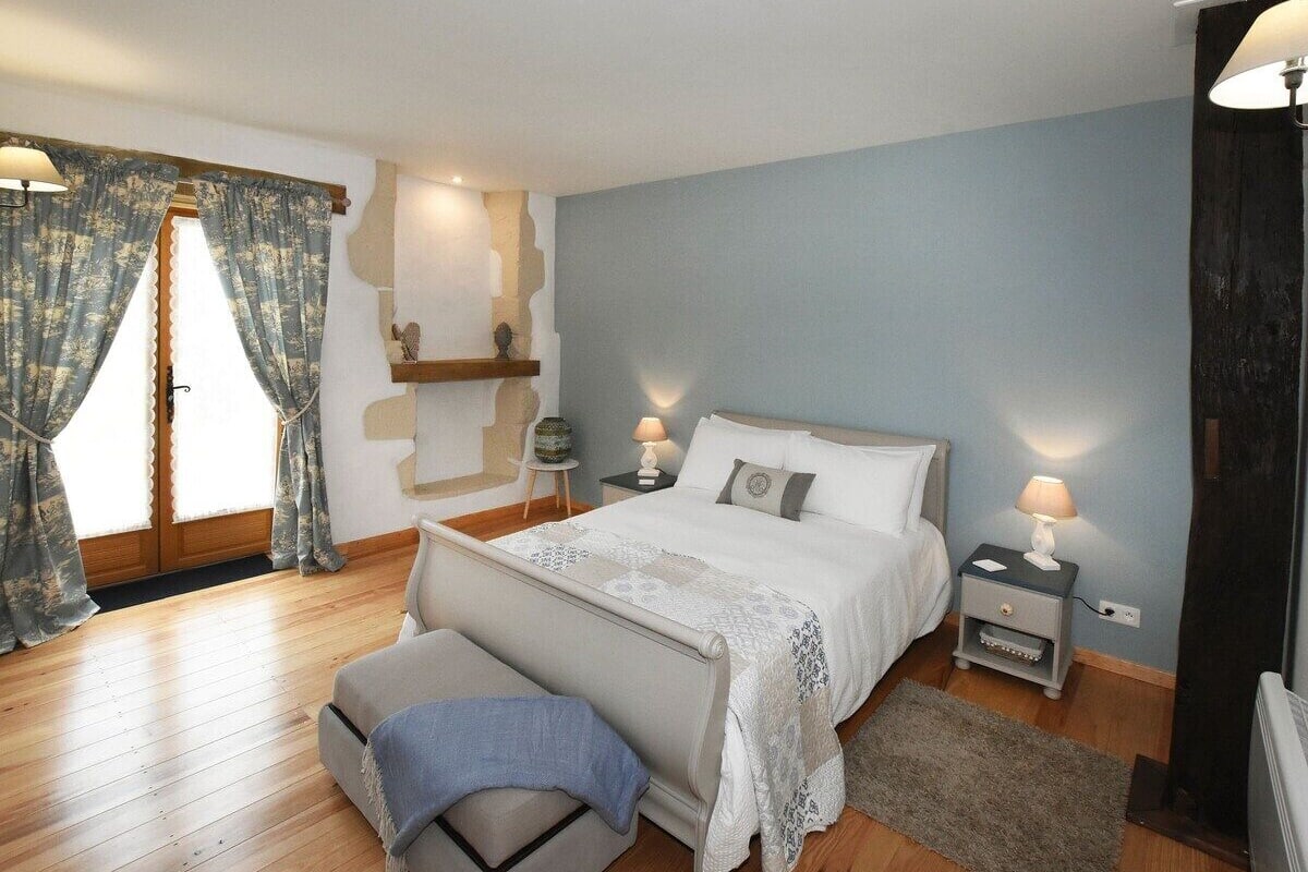 Un dormitorio con cama, mesitas de noche, un banco y una ventana con cortinas.