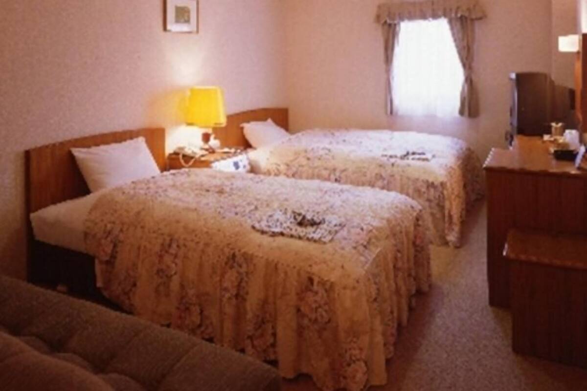 A hotel room with two beds, a desk, a chair, and a lamp.