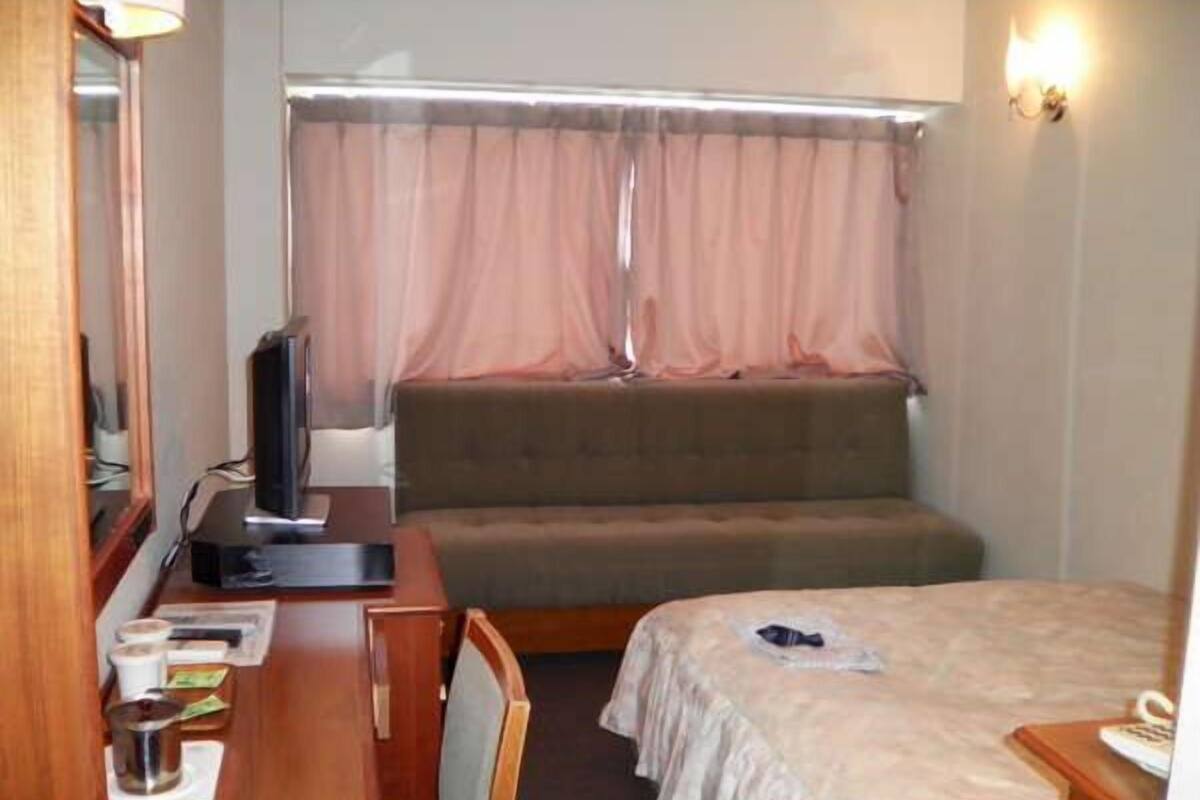 A compact room with a bed, a small desk, a television, and a window with curtains.