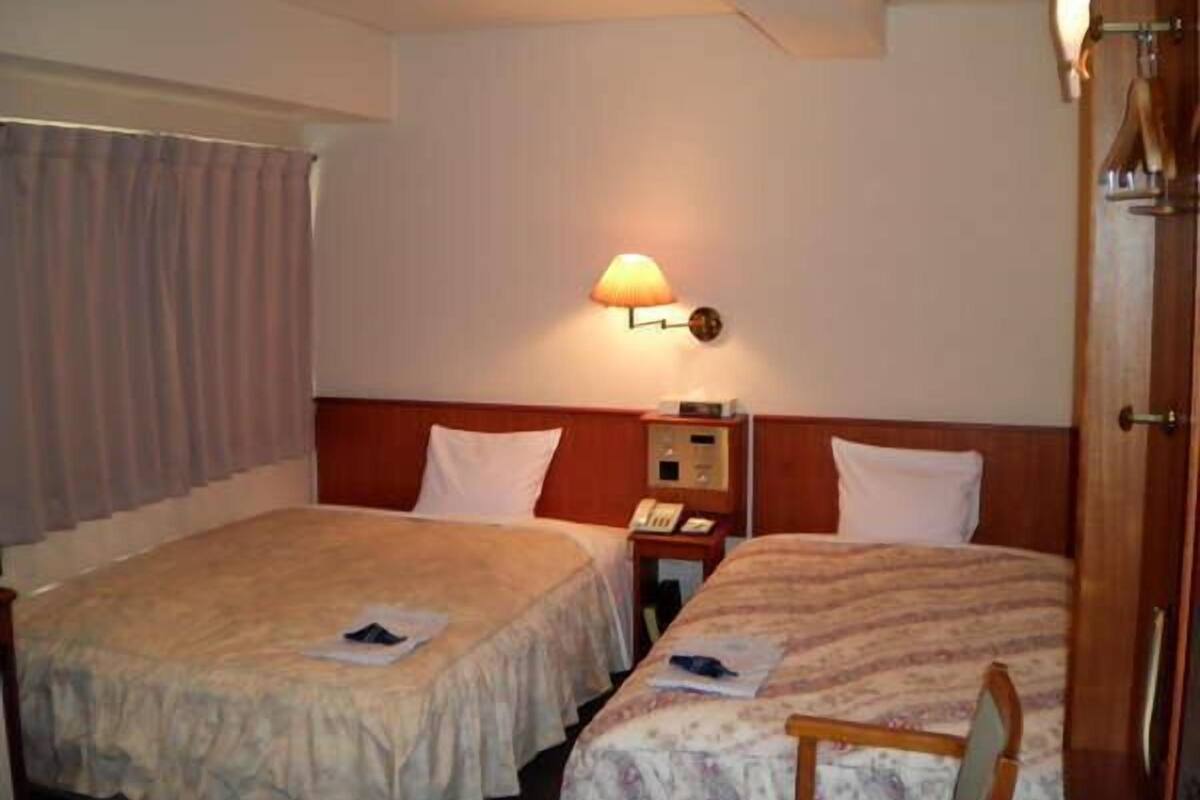 A hotel room with two beds, a nightstand with a lamp, and a window with curtains.