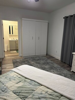 A bedroom with a bed, a grey rug, a wardrobe, and a bathroom visible through an open door. - Cozy 6-Person Cottage Near I-75 (Sumner)