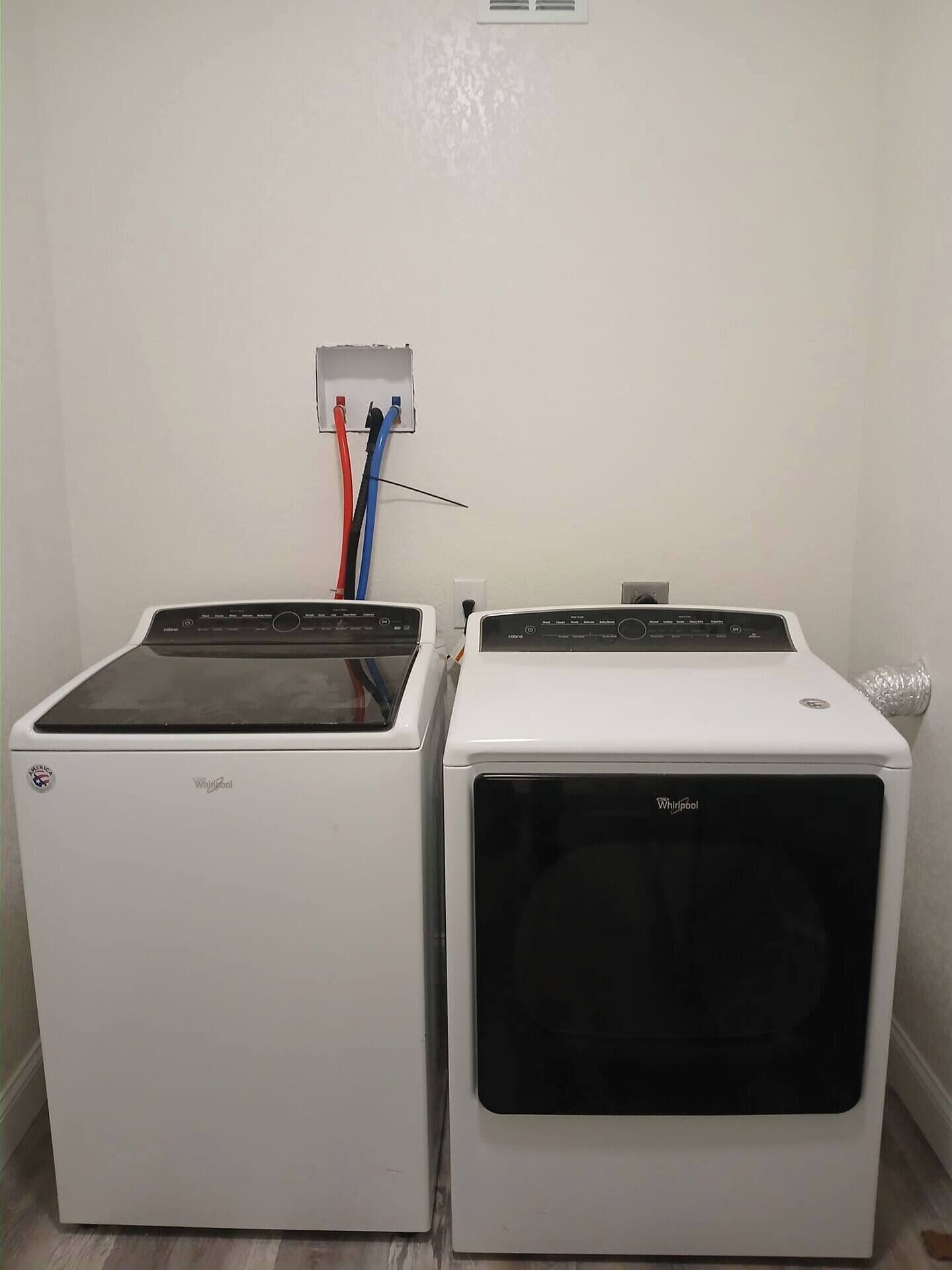Dues sequedores Whirlpool blanques una al costat de l'altra, amb una presa d'electricitat i cables a la part superior.