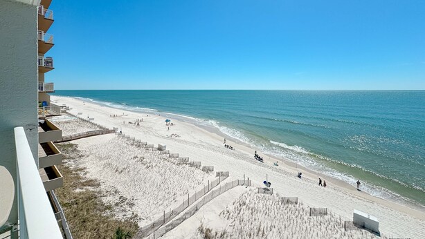 Une vue sur la plage depuis un balcon, avec un ciel dégagé, une plage de sable et l’océan.