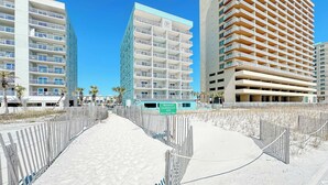 Un hôtel situé en bord de mer, avec plusieurs étages, des balcons et une promenade piétonne de sable.