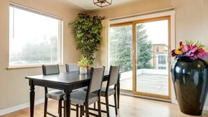 Un coin repas avec une grande table, des chaises, une plante en pot et un vase rempli de fleurs.